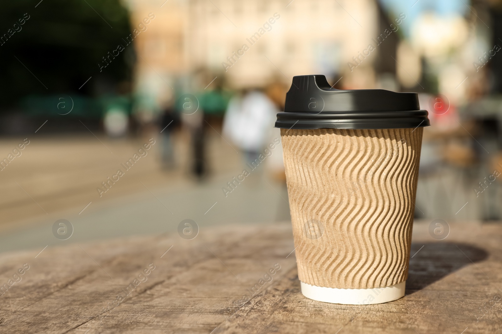 Photo of Cardboard takeaway coffee cup with plastic lid on wooden table in city, space for text