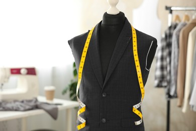 Photo of Mannequin with unfinished suit jacket and measuring tape in tailor shop, space for text