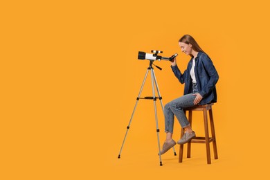 Photo of Young astronomer looking at stars through telescope on orange background, space for text