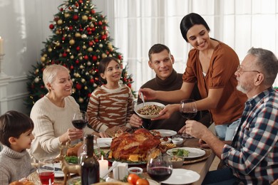 Photo of Woman with bowl of traditional Christmas kutia and her family during festive dinner at home. Slavic dish