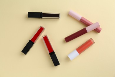 Different lip glosses on pale yellow background, flat lay