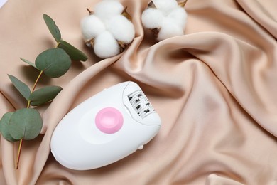 Photo of Modern epilator, fluffy cotton flowers and eucalyptus branch on silk fabric, above view. Space for text