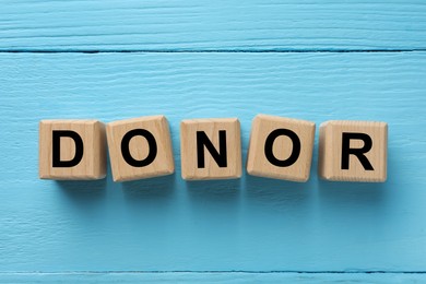 Photo of Cubes with word Donor on light blue wooden table, flat lay