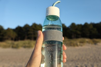Photo of Woman holding glass bottle with water on beach, closeup