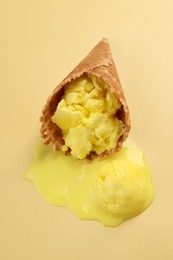 Photo of Melted ice cream in wafer cone on pale yellow background