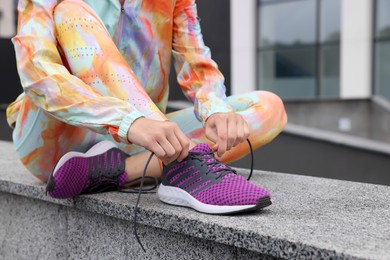 Photo of Woman in gym clothes tying shoelace of sneakers on street, closeup. Space for text