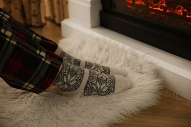 Photo of Woman in warm socks sitting near fireplace with burning wood at home, closeup