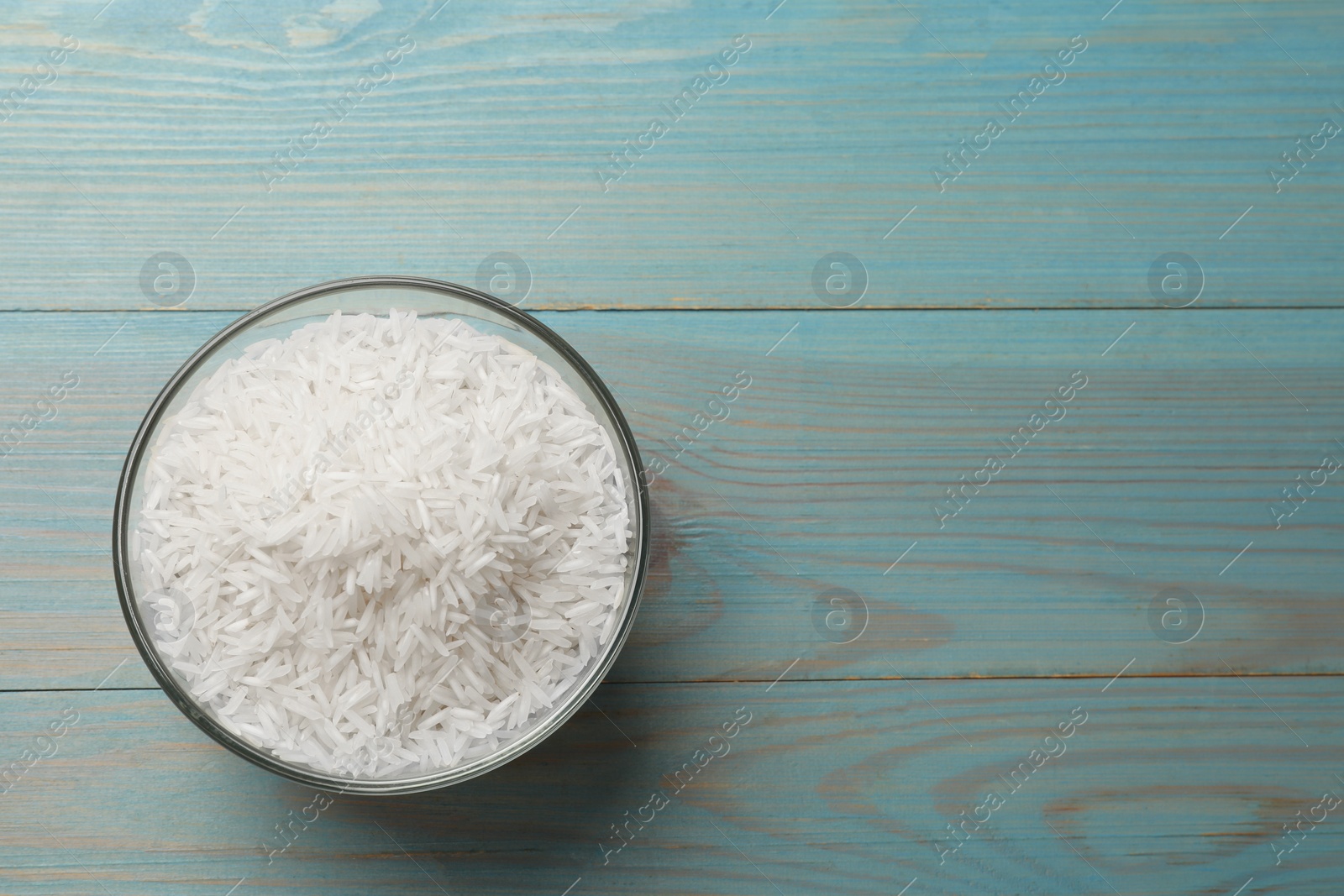 Photo of Raw basmati rice in bowl on light blue wooden table, top view. Space for text