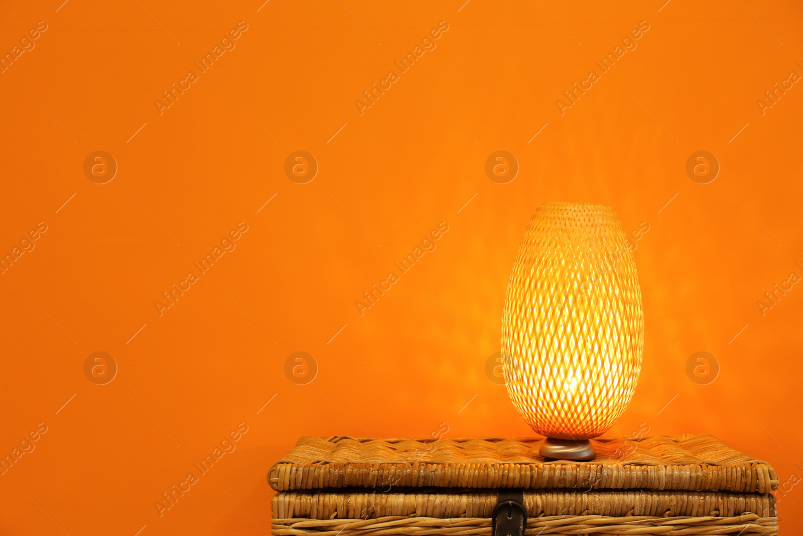 Photo of Modern lamp on wicker chest against color background. Space for text