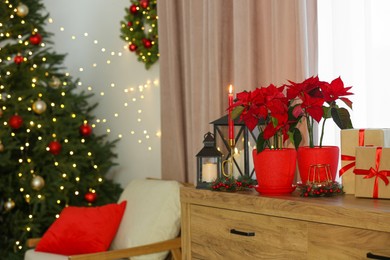 Photo of Potted poinsettias, burning candles and festive decor on dresser in room, space for text. Christmas traditional flower