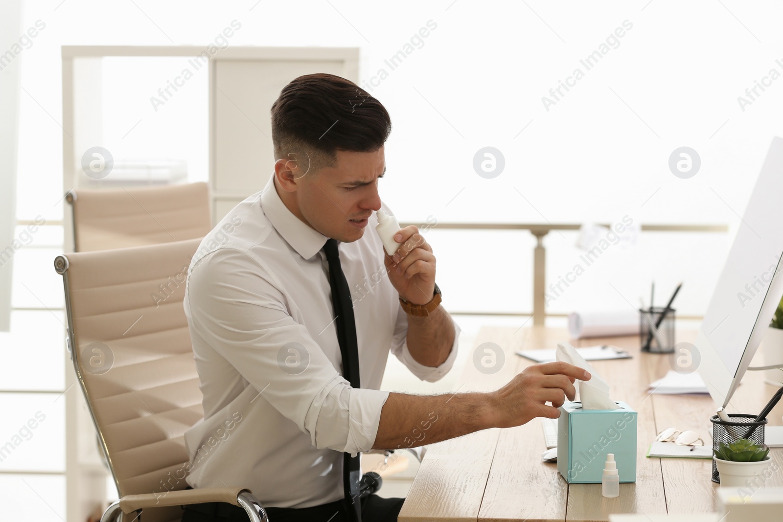 Photo of Ill businessman using nasal spray at table in office