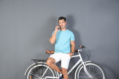 Photo of Handsome young hipster man with bicycle and phone on color background
