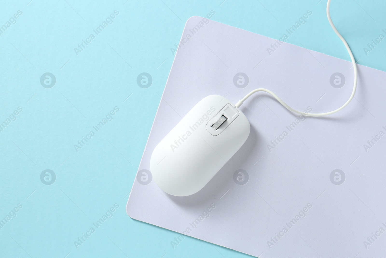 Photo of Wired mouse and mousepad on light blue background, top view. Space for text
