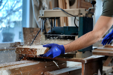 Photo of Professional carpenter working with grinding machine in shop, closeup