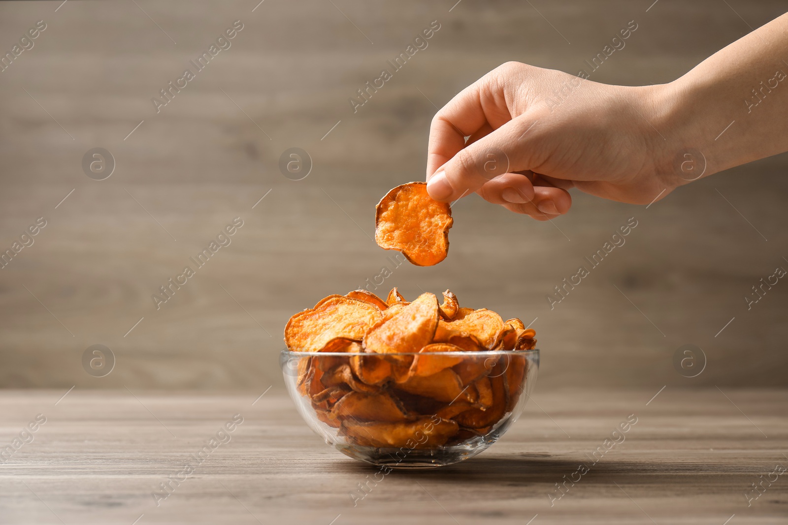 Photo of Woman taking sweet potato chip from bowl on table, closeup