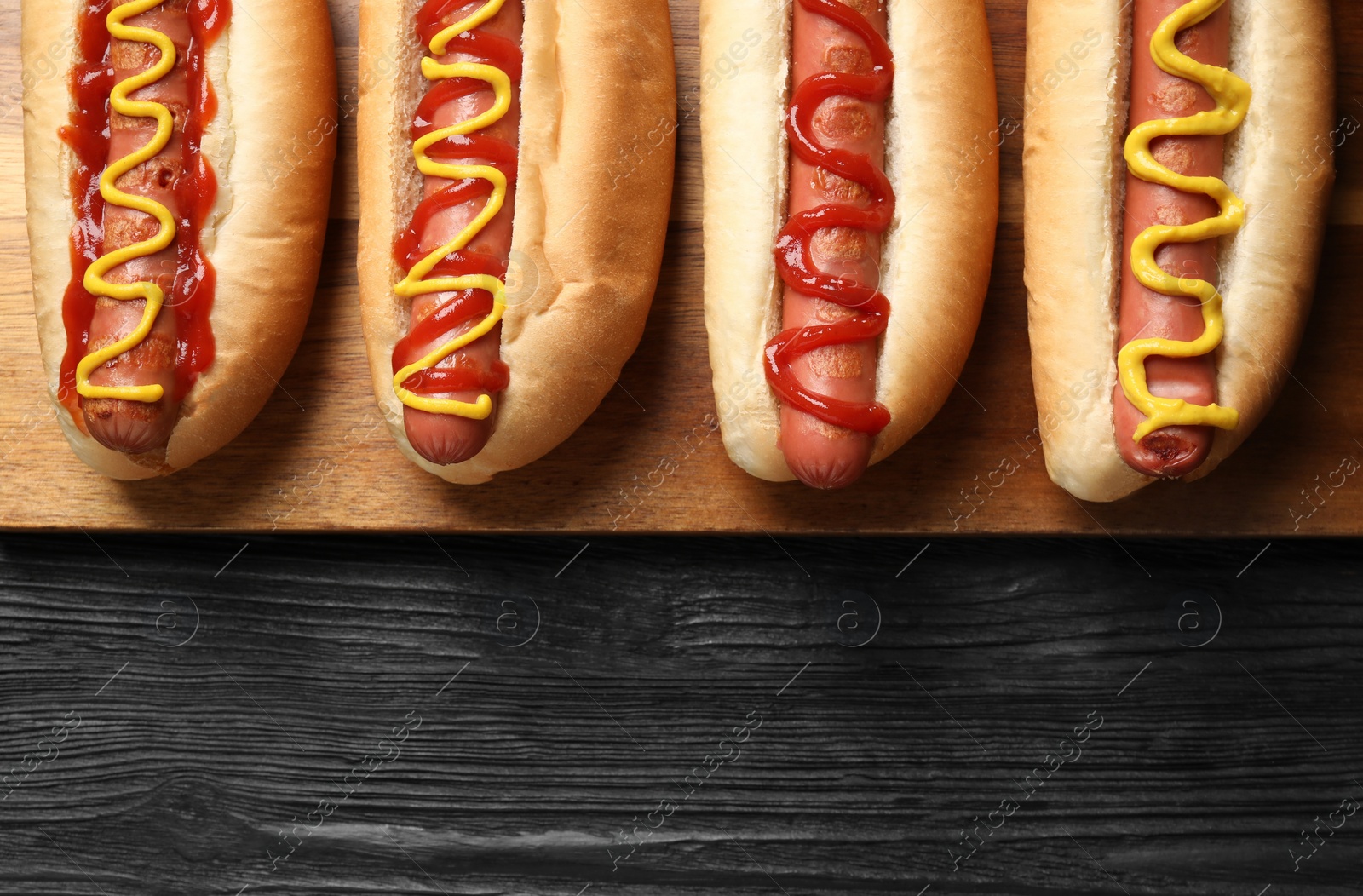 Photo of Delicious hot dogs with mustard and ketchup on black wooden table, top view. Space for text