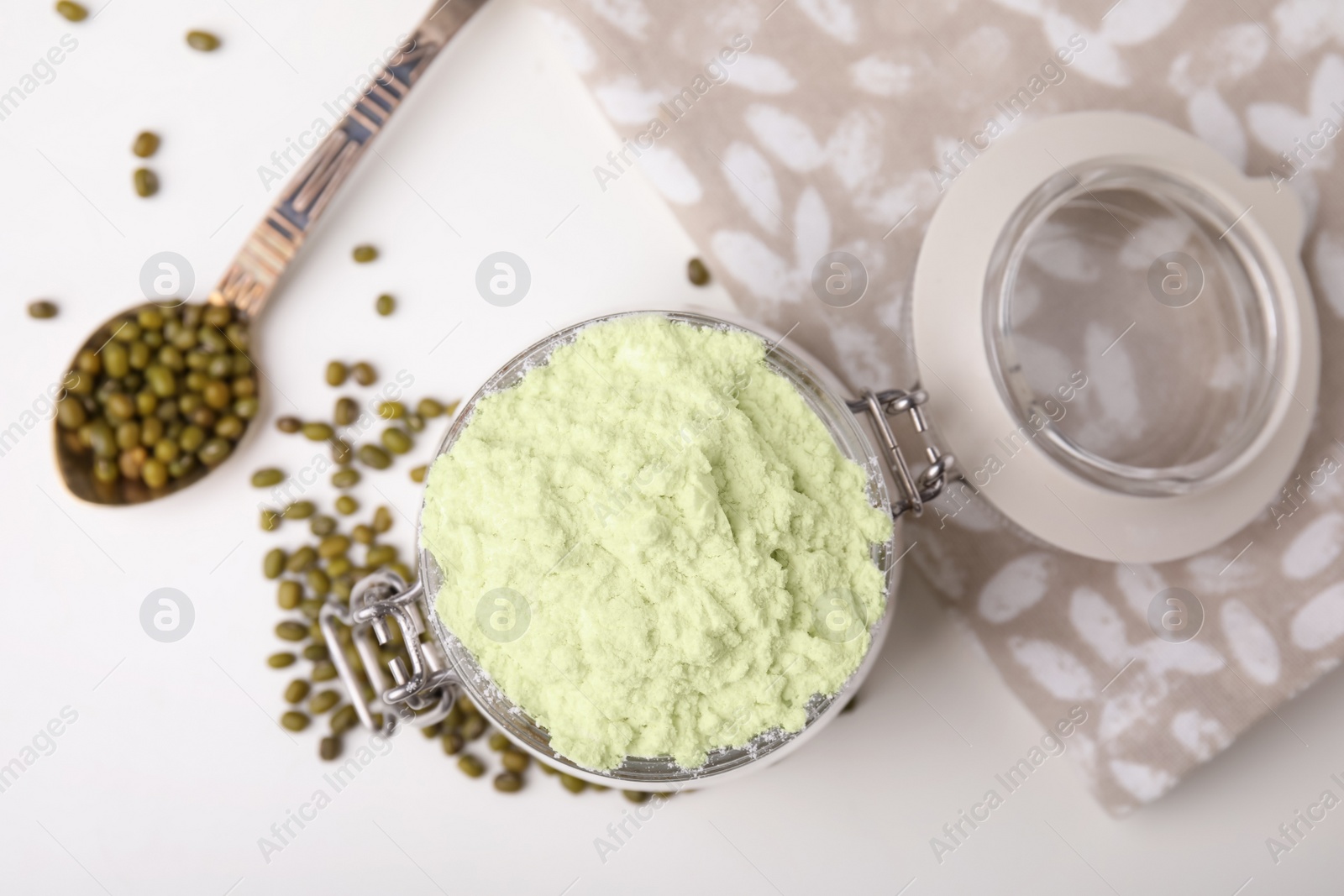 Photo of Glass jar with flour, spoon and mung beans on white table, flat lay