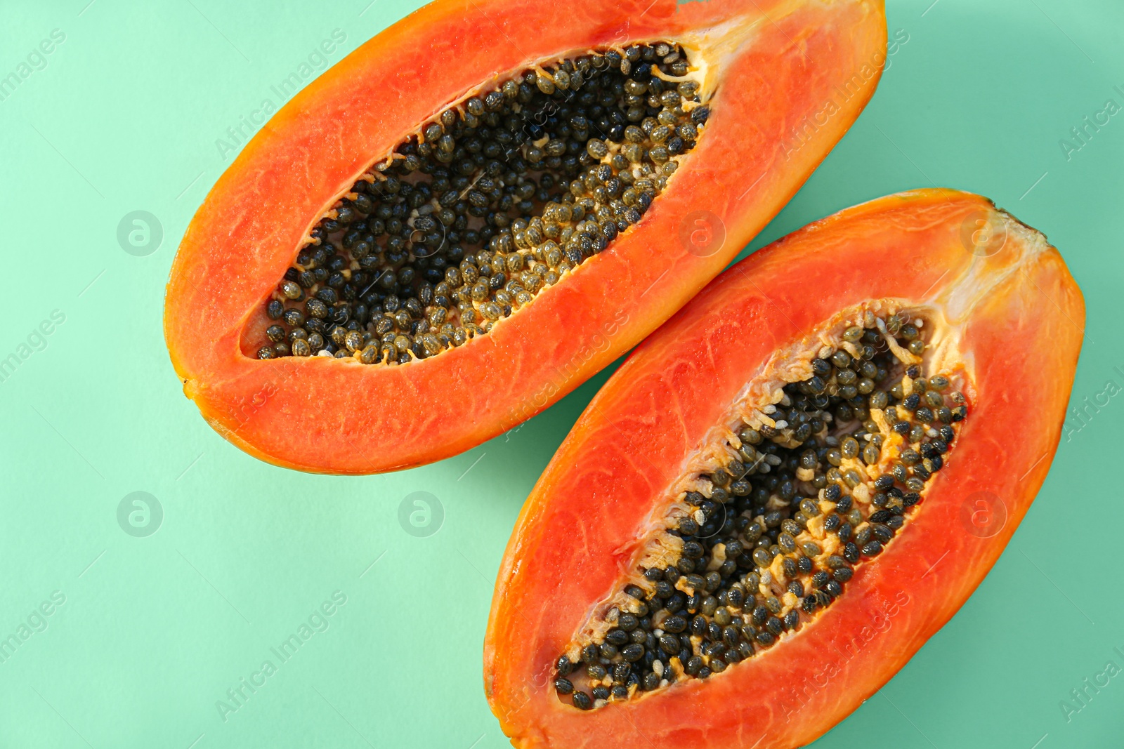 Photo of Halves of fresh ripe papaya on light turquoise background, flat lay. Exotic fruit