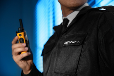 Professional security guard with portable radio set near window in dark room, closeup