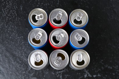 Photo of Energy drinks in wet cans on black textured table, flat lay. Functional beverage