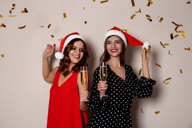 Photo of Happy women in Santa hats with champagne and confetti on beige background. Christmas party