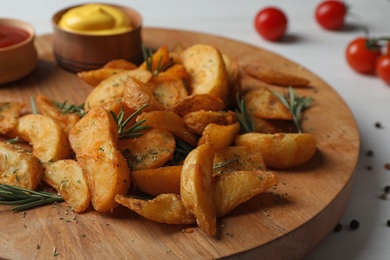 Photo of Wooden board with baked potatoes and rosemary on table, closeup