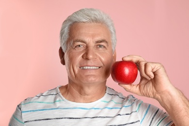 Photo of Mature man with healthy teeth and apple on color background