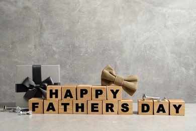 Photo of Cubes with phrase Happy Father's Day, bow tie and gift box on grey background. Space for text