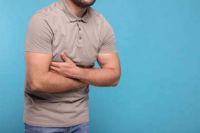 Photo of Man suffering from stomach pain on light blue background, closeup and space for text