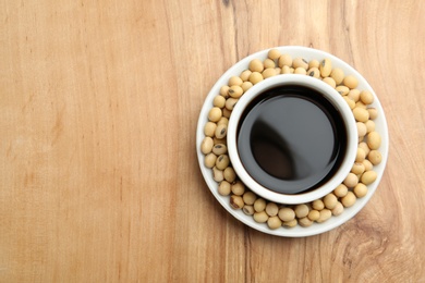 Photo of Dish of soy sauce with beans on wooden background, top view. Space for text