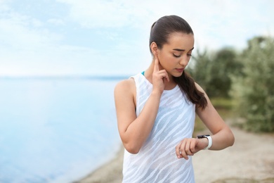 Photo of Young woman checking pulse after training on beach. Space for text