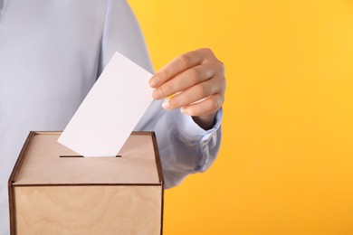 Photo of Woman putting her vote into ballot box on orange background, closeup. Space for text