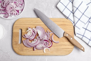 Wooden board with cut fresh red onion and knife on grey marble table, flat lay