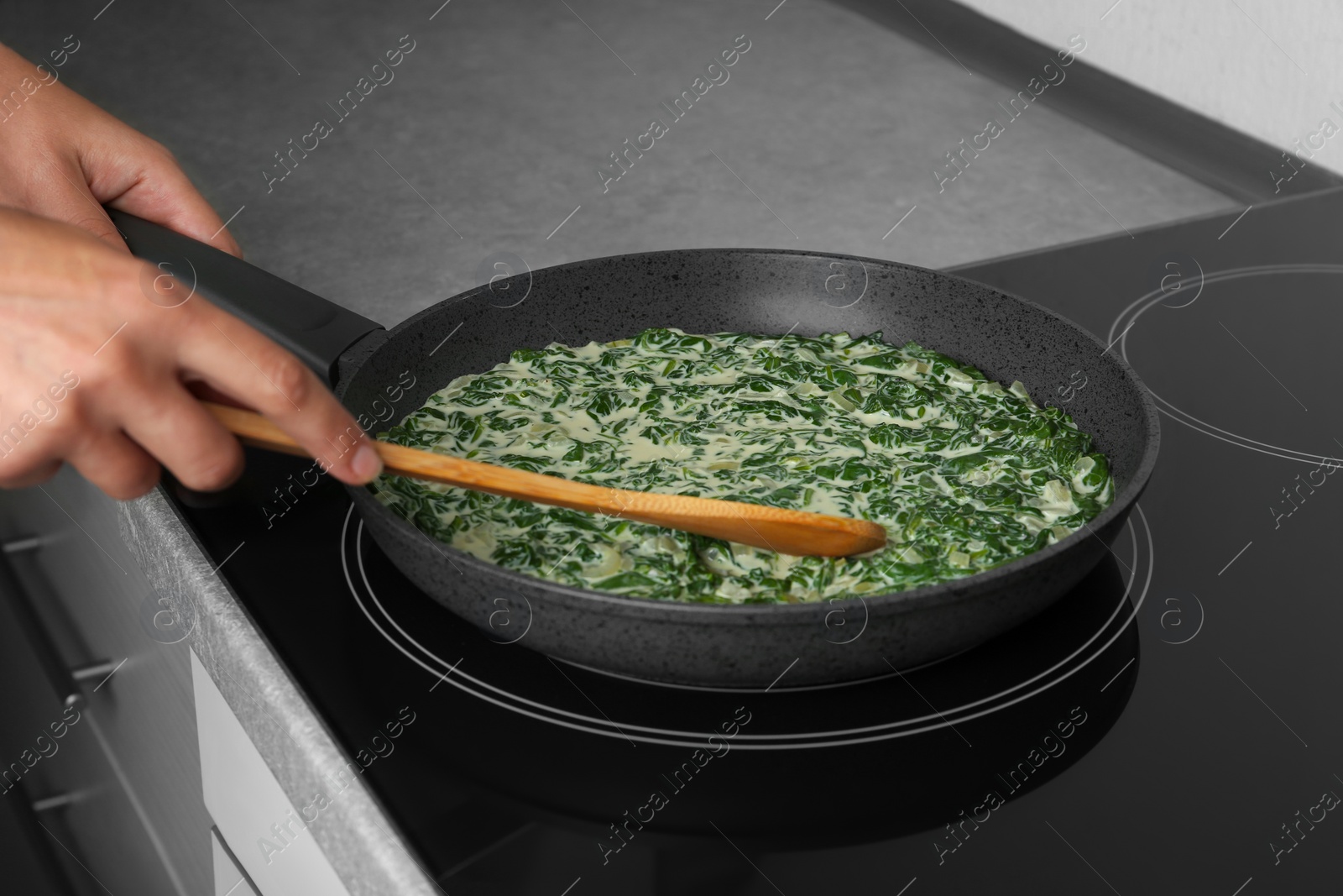 Photo of Woman cooking tasty spinach dip on kitchen stove, closeup view