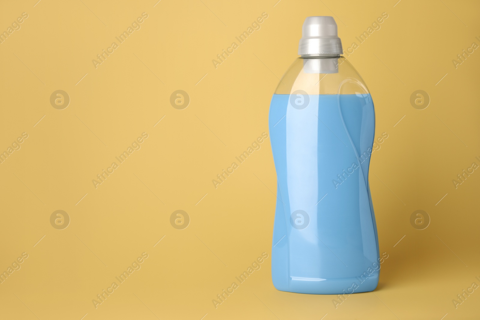 Photo of Bottle of fabric softener on pale yellow background, space for text