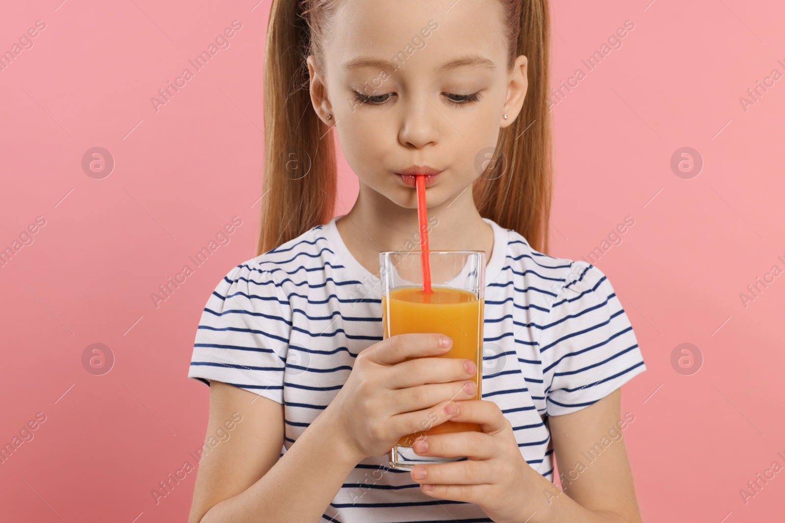 Photo of Little girl drinking fresh juice on pink background