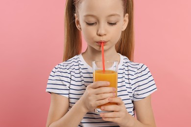 Little girl drinking fresh juice on pink background