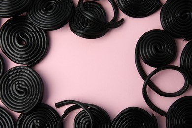 Photo of Frame of tasty black liquorice candies on pink background, flat lay. Space for text