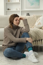 Photo of Sad young woman sitting on floor at home