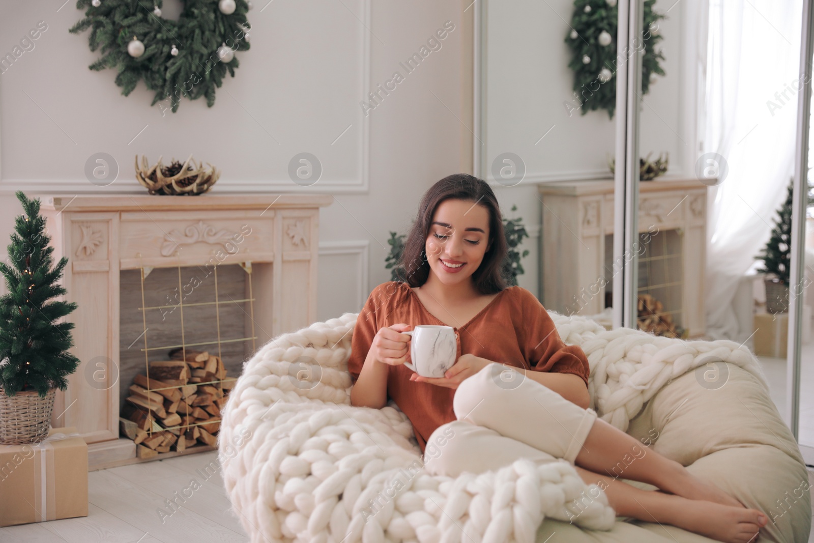 Photo of Woman with hot drink resting in comfortable papasan chair at home