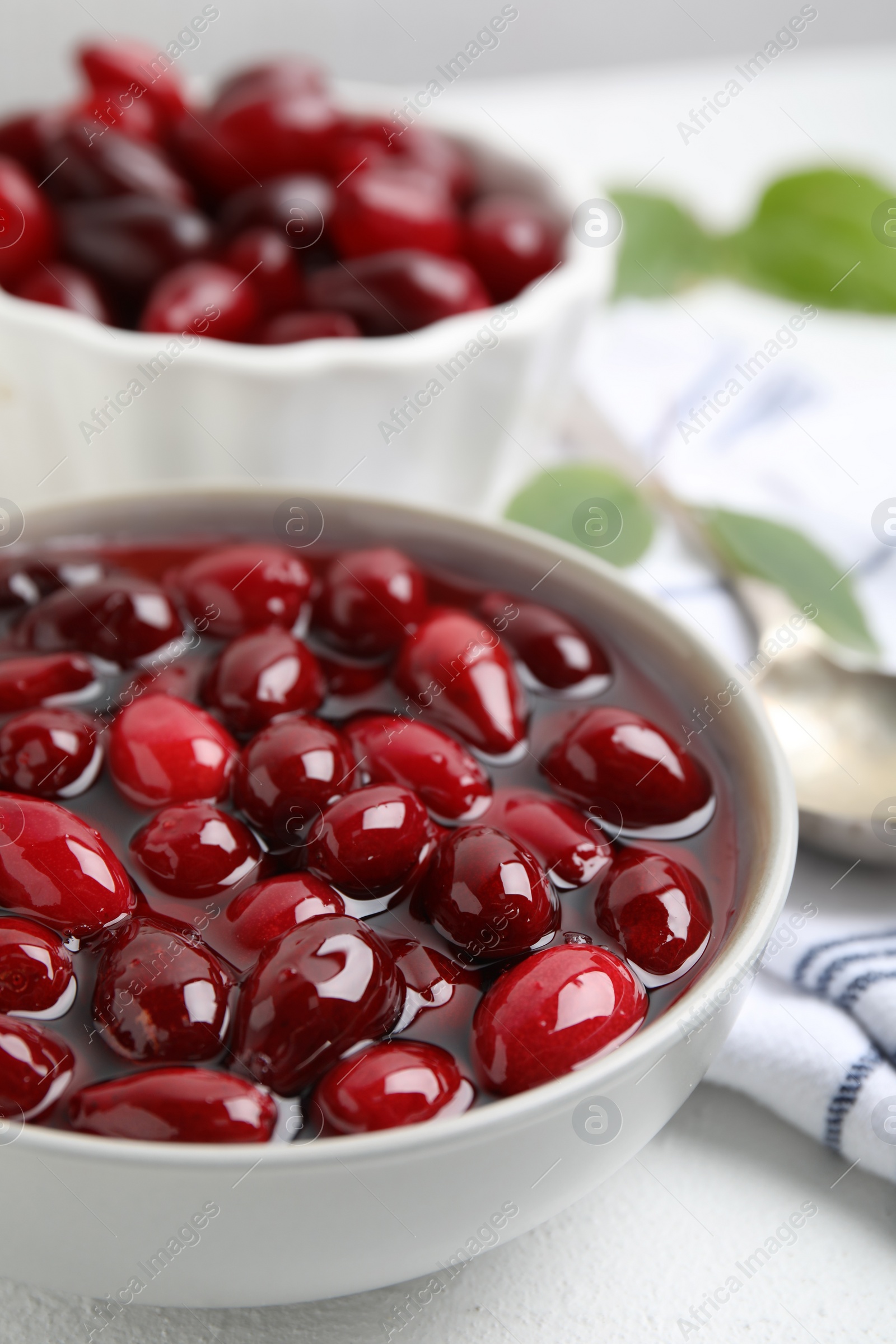 Photo of Delicious dogwood jam with berries in bowl on white table, closeup