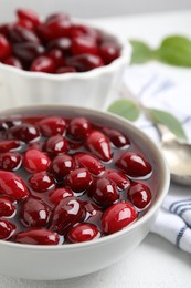 Photo of Delicious dogwood jam with berries in bowl on white table, closeup