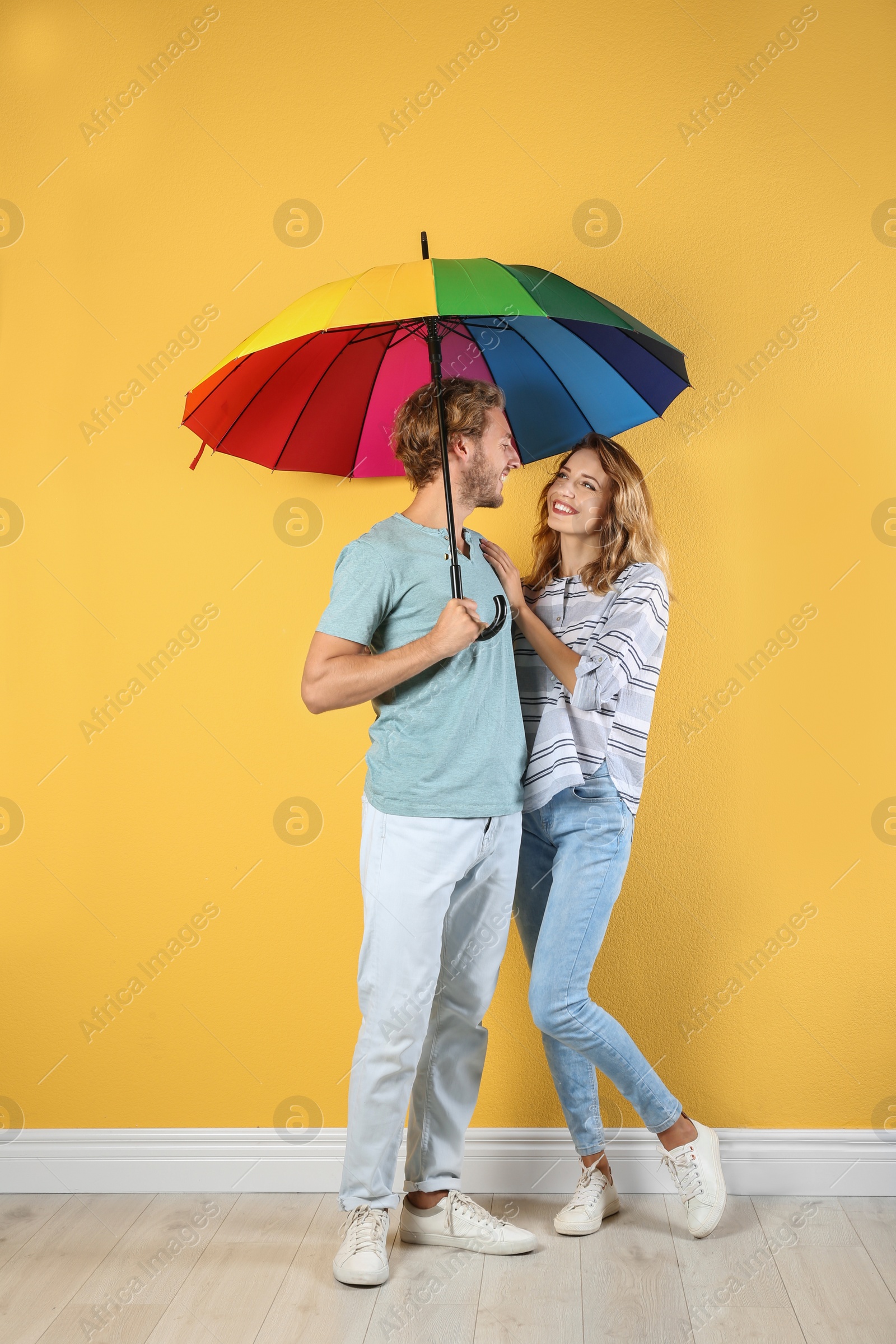 Photo of Couple with rainbow umbrella near color wall