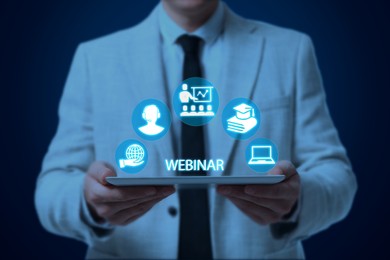Image of Webinar. Man holding tablet on dark blue background, closeup. Virtual screen with icons over computer