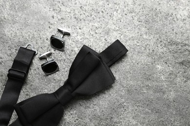 Photo of Stylish black bow tie and cufflinks on grey stone background, flat lay. Space for text