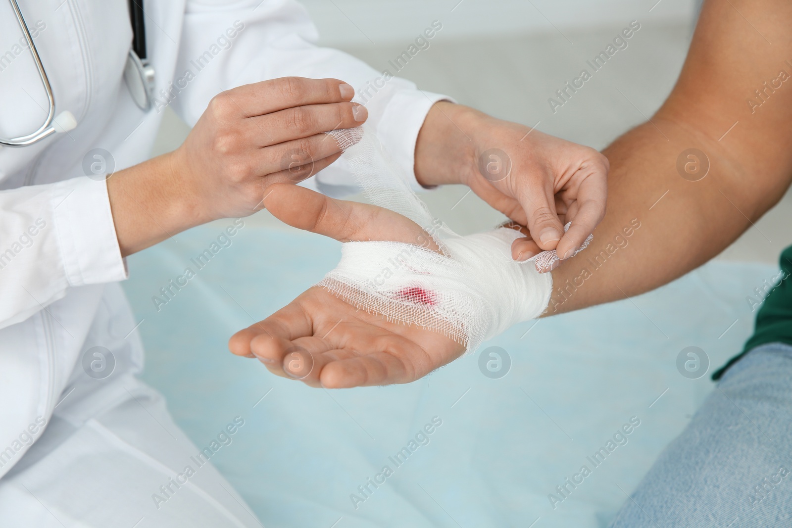 Photo of Female doctor applying bandage on young man's hand in clinic, closeup. First aid