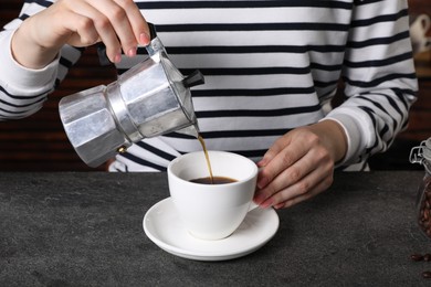 Woman pouring aromatic coffee from moka pot into cup at grey table indoors, closeup