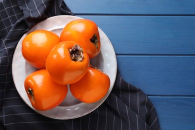 Photo of Delicious ripe persimmons on blue wooden table, top view. Space for text