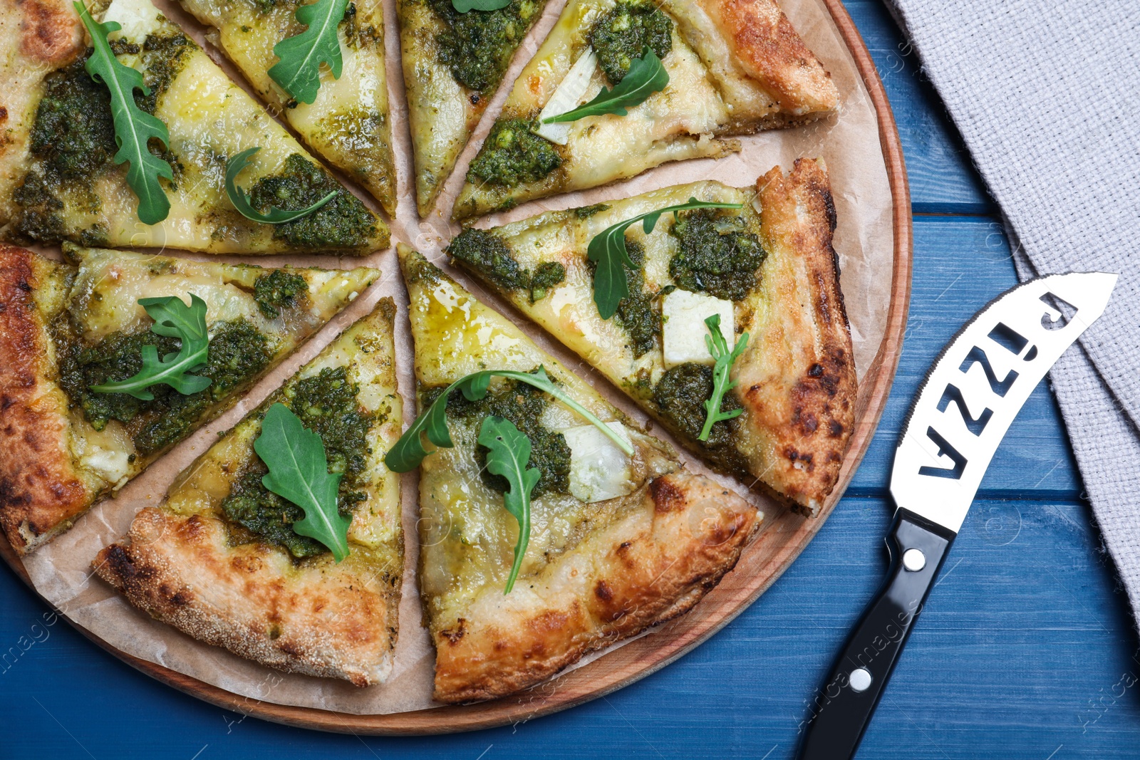 Photo of Delicious pizza with pesto, cheese and arugula served on blue wooden table, flat lay