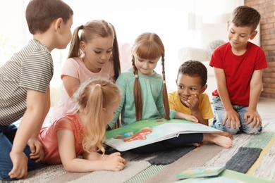 Photo of Cute little children reading book together indoors. Learning by playing